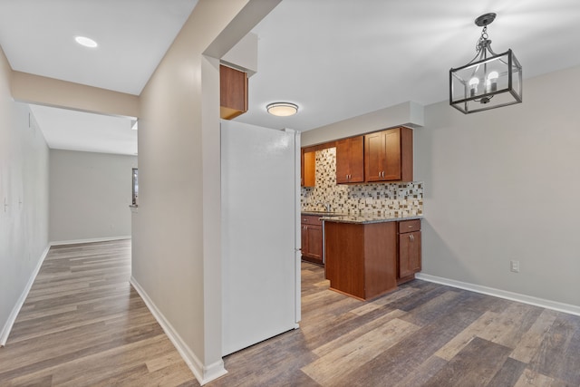 kitchen featuring white refrigerator, hanging light fixtures, decorative backsplash, a notable chandelier, and dark hardwood / wood-style flooring