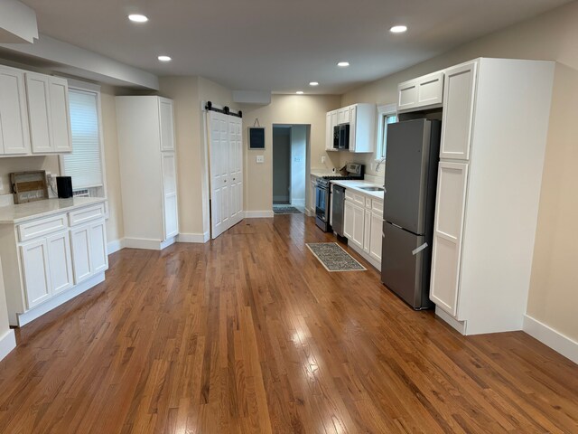 kitchen featuring a barn door, appliances with stainless steel finishes, light stone counters, dark hardwood / wood-style floors, and white cabinets