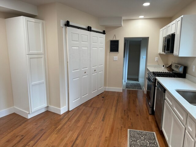 kitchen with a barn door, appliances with stainless steel finishes, hardwood / wood-style flooring, sink, and white cabinetry