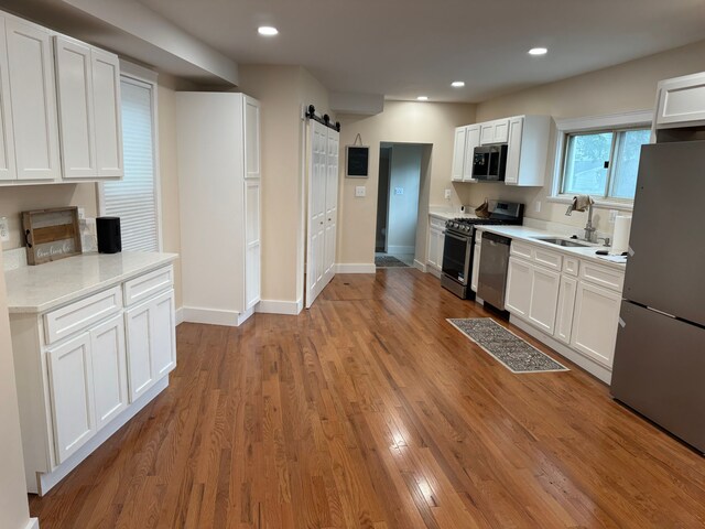 kitchen with sink, white cabinets, light hardwood / wood-style flooring, a barn door, and appliances with stainless steel finishes