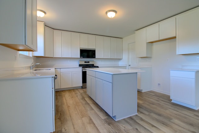 kitchen with sink, appliances with stainless steel finishes, white cabinets, a kitchen island, and light wood-type flooring