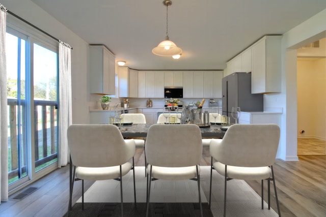 kitchen featuring white cabinetry, hanging light fixtures, light wood-type flooring, and appliances with stainless steel finishes