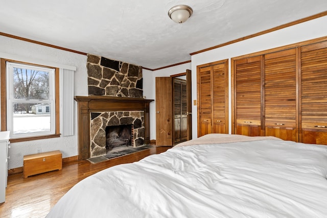 bedroom featuring a stone fireplace, wood-type flooring, ornamental molding, and two closets