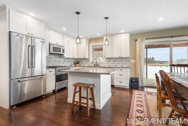 kitchen with white cabinetry, light stone countertops, hanging light fixtures, high quality appliances, and a kitchen island