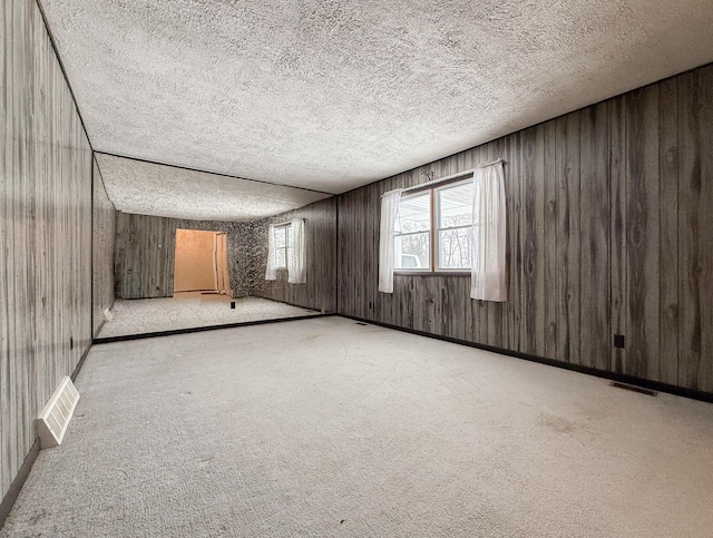 unfurnished room with wood walls, light colored carpet, and a textured ceiling