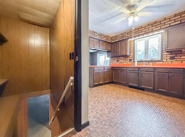 kitchen with a textured ceiling, ceiling fan, wooden walls, and sink