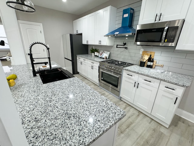 kitchen featuring light stone countertops, white cabinets, wall chimney range hood, and appliances with stainless steel finishes