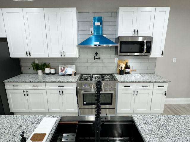 kitchen featuring backsplash, white cabinets, light stone countertops, range hood, and stainless steel appliances