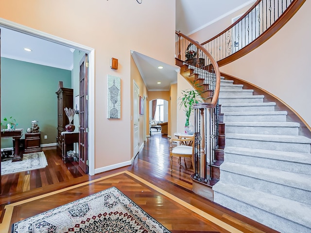 foyer entrance with crown molding, hardwood / wood-style flooring, baseboards, stairway, and arched walkways