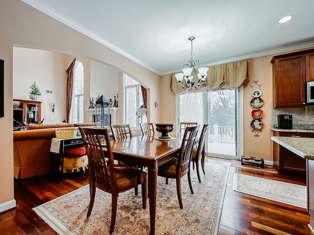 dining room featuring an inviting chandelier, plenty of natural light, ornamental molding, arched walkways, and wood finished floors