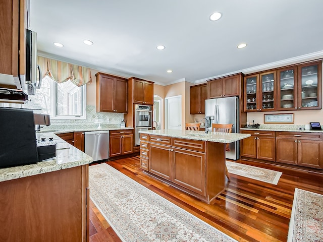 kitchen with dark wood-type flooring, light stone countertops, a kitchen island with sink, a breakfast bar area, and appliances with stainless steel finishes