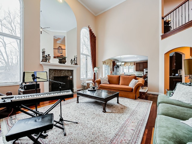 living room with ceiling fan with notable chandelier, a high ceiling, hardwood / wood-style flooring, and crown molding