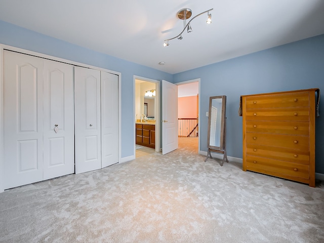 unfurnished bedroom with light carpet, baseboards, a closet, and ensuite bath