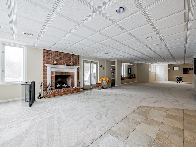 unfurnished living room with carpet flooring, a fireplace, baseboards, visible vents, and a drop ceiling