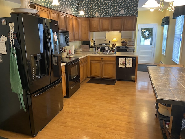 kitchen featuring sink, hanging light fixtures, kitchen peninsula, light hardwood / wood-style floors, and black appliances