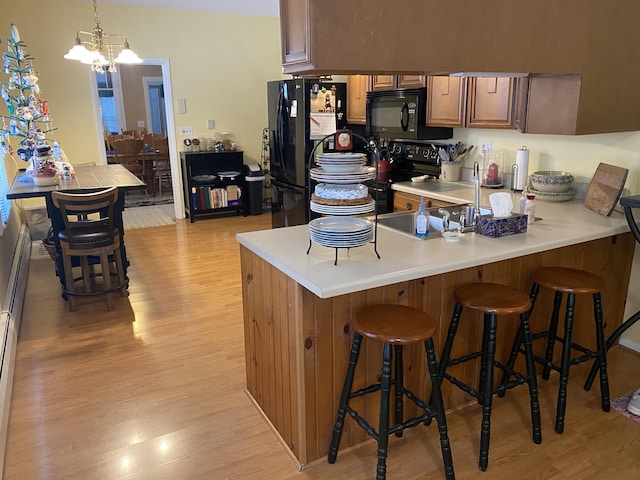 kitchen featuring a notable chandelier, kitchen peninsula, pendant lighting, a kitchen bar, and black appliances