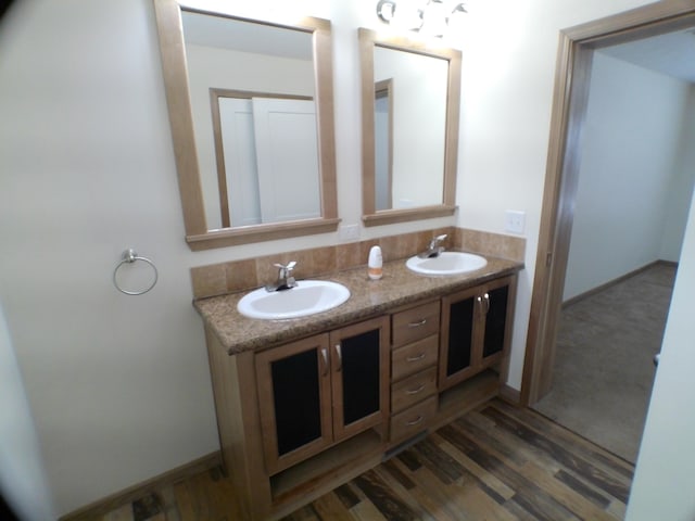 full bathroom featuring wood finished floors, a sink, baseboards, and double vanity