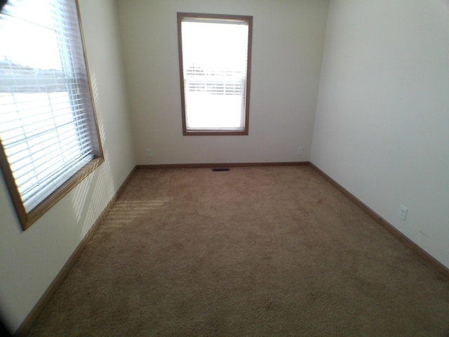 unfurnished room with carpet, visible vents, baseboards, and a wealth of natural light