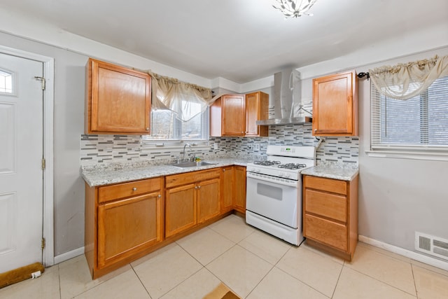 kitchen with decorative backsplash, wall chimney range hood, white gas stove, light stone countertops, and sink