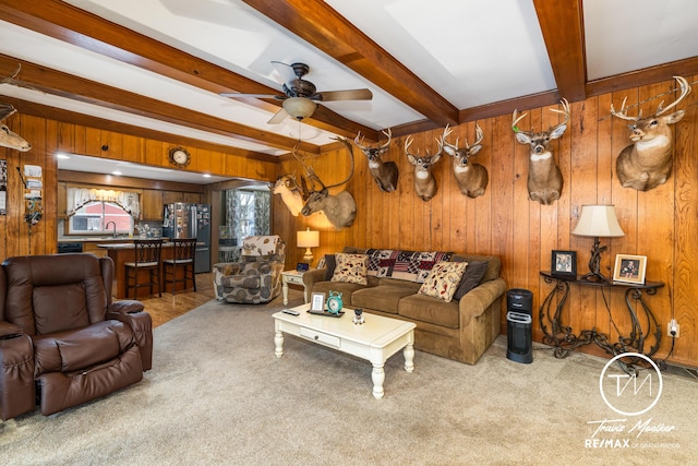 living room featuring ceiling fan, sink, beamed ceiling, wood walls, and carpet