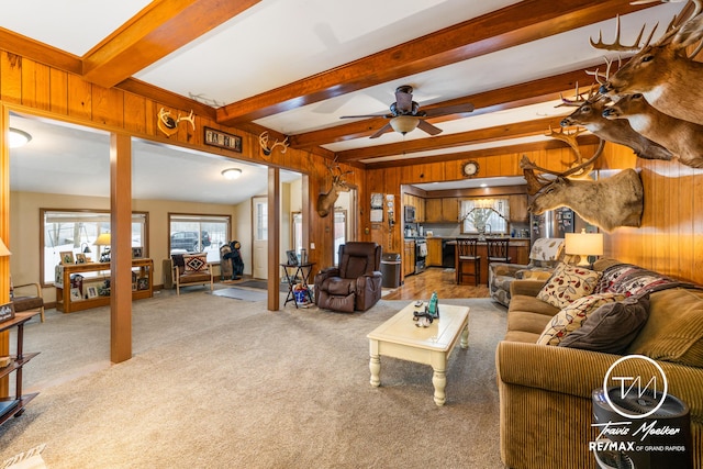 living room featuring beam ceiling, wood walls, ceiling fan, and light carpet