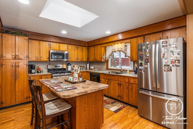 kitchen with a center island, sink, a skylight, appliances with stainless steel finishes, and a breakfast bar area