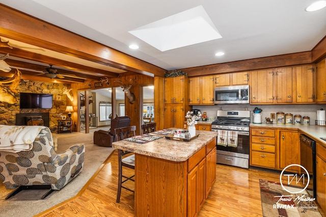 kitchen with a skylight, ceiling fan, a center island, stainless steel appliances, and beamed ceiling