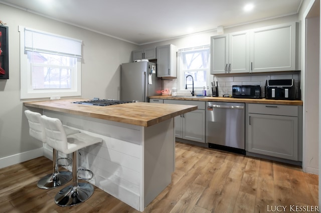 kitchen featuring butcher block countertops, gray cabinets, stainless steel appliances, decorative backsplash, and sink