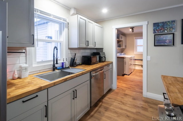 kitchen with stainless steel dishwasher, wood counters, tasteful backsplash, and washing machine and clothes dryer