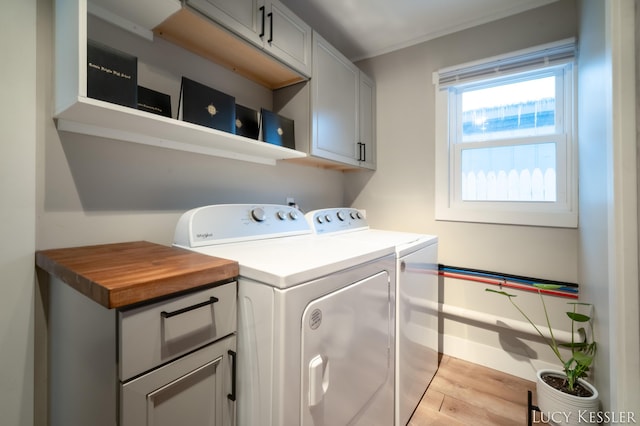 laundry area featuring light wood-type flooring, washing machine and clothes dryer, and cabinets