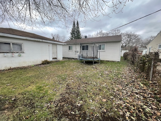 rear view of house with a yard and a trampoline