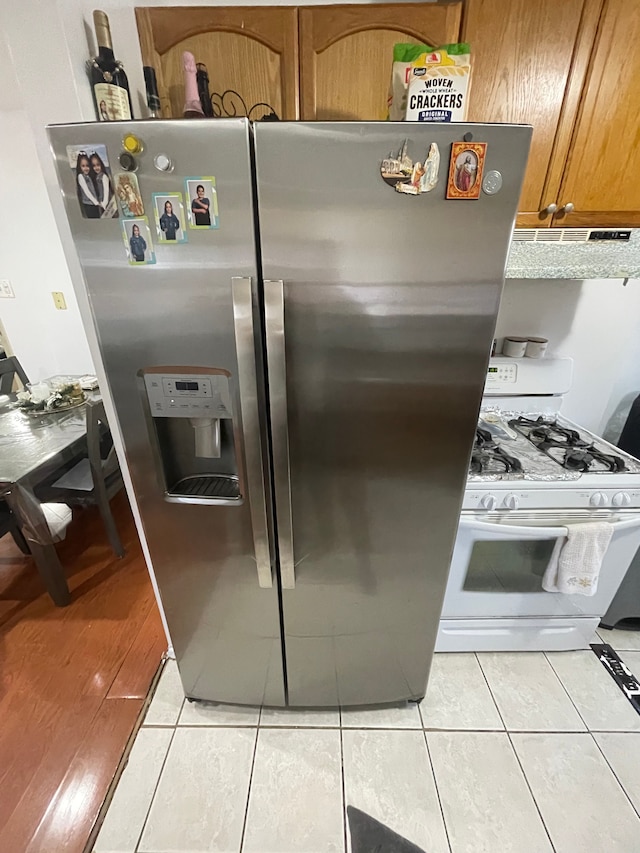 kitchen with white gas range, light tile patterned flooring, extractor fan, and stainless steel refrigerator with ice dispenser