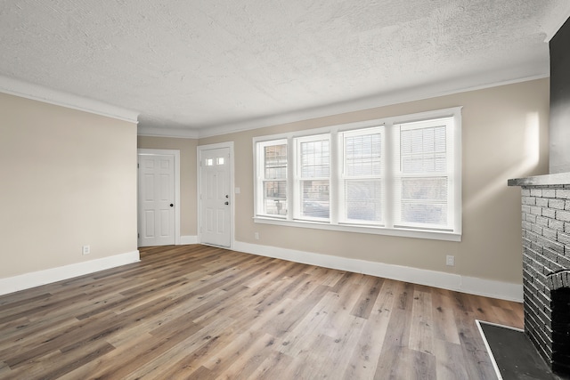 unfurnished living room featuring crown molding, a brick fireplace, a textured ceiling, and light hardwood / wood-style flooring