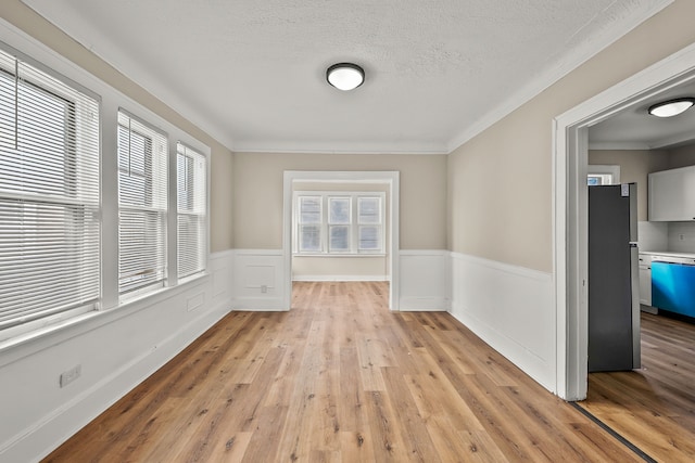 spare room featuring crown molding, a textured ceiling, and light wood-type flooring