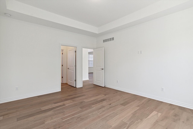 unfurnished bedroom with a raised ceiling and light hardwood / wood-style floors