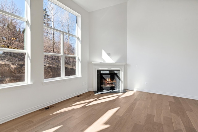 unfurnished living room with a high end fireplace, light wood-type flooring, and a wealth of natural light