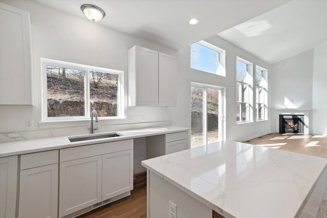 kitchen featuring a center island, white cabinets, sink, hardwood / wood-style flooring, and light stone counters