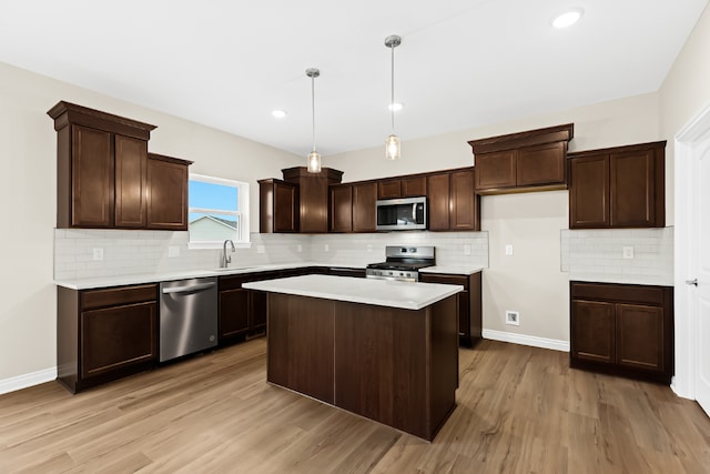 kitchen with a center island, stainless steel appliances, light countertops, hanging light fixtures, and a sink