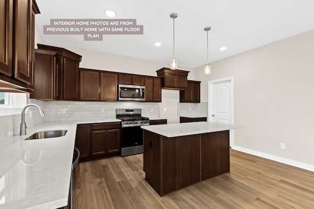 kitchen featuring decorative light fixtures, appliances with stainless steel finishes, a kitchen island, a sink, and light stone countertops