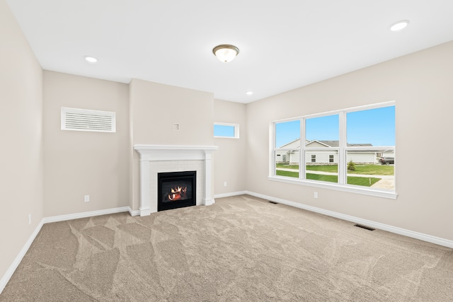 unfurnished living room with carpet floors, baseboards, visible vents, and a glass covered fireplace