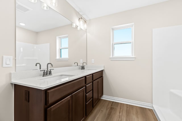 full bath featuring double vanity, wood finished floors, a sink, and baseboards