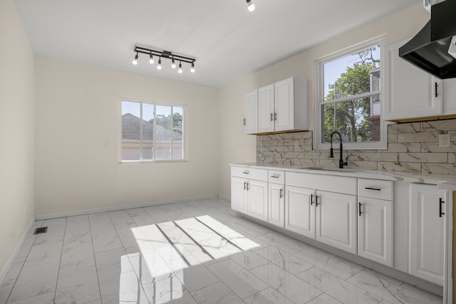 kitchen featuring decorative backsplash, wall chimney range hood, white cabinets, and sink