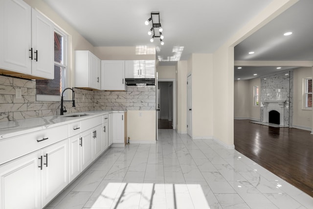 kitchen featuring light stone countertops, white cabinetry, tasteful backsplash, sink, and a large fireplace