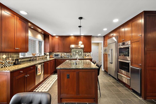 kitchen with stainless steel appliances, a kitchen island, pendant lighting, and dark stone counters