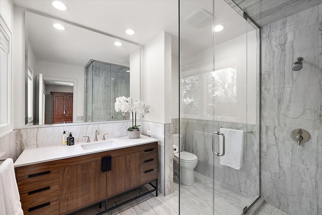 bathroom with tile walls, an enclosed shower, vanity, and toilet