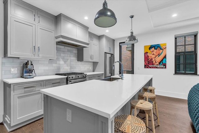 kitchen with stainless steel appliances, gray cabinets, light countertops, dark wood-type flooring, and a kitchen island with sink