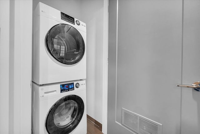 clothes washing area with laundry area, visible vents, stacked washer / dryer, and wood finished floors