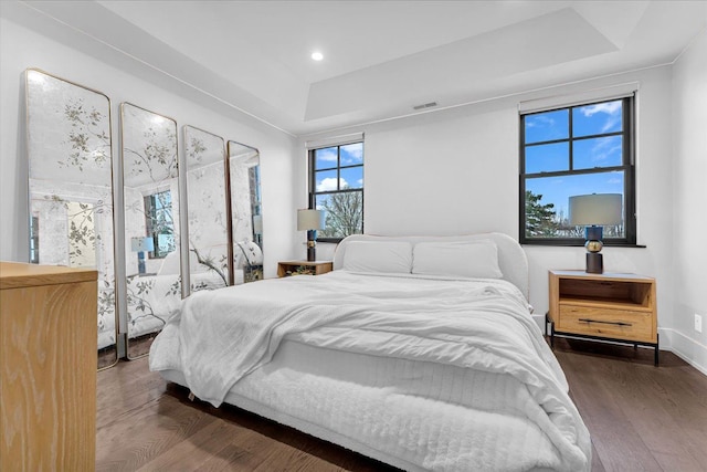 bedroom featuring a tray ceiling, dark wood-style flooring, recessed lighting, visible vents, and baseboards