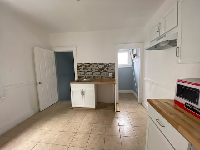 kitchen featuring wooden counters, decorative backsplash, sink, white cabinets, and light tile patterned flooring