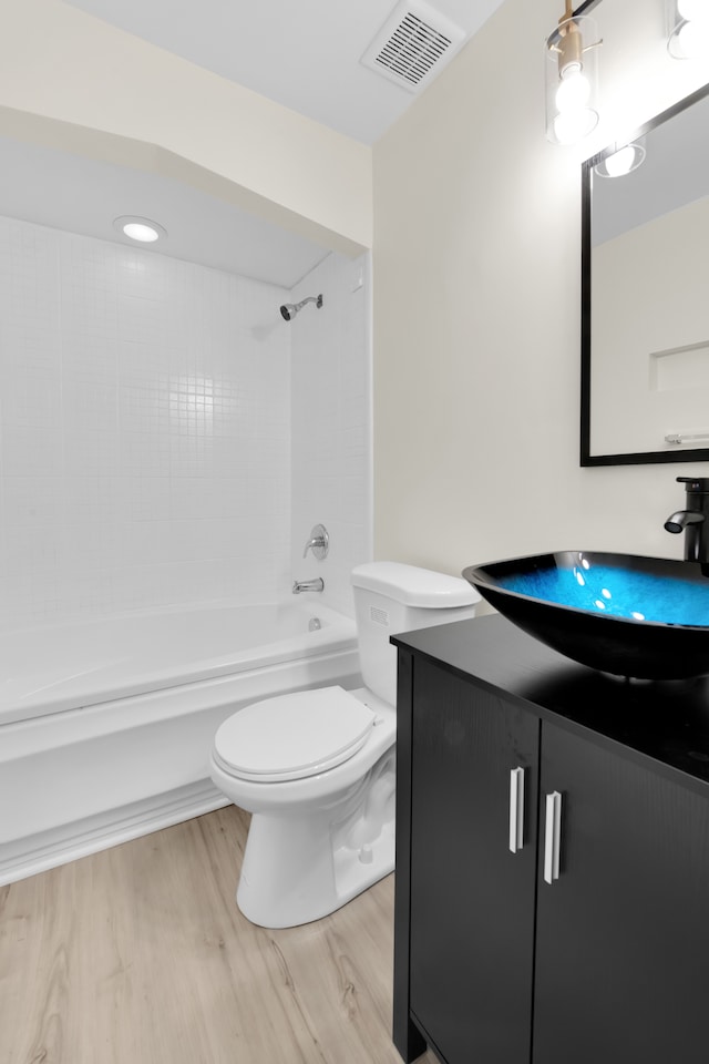 full bathroom with toilet, tiled shower / bath, vanity, and hardwood / wood-style floors